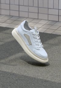 Weiße Leder-Sneaker mit einer abgerundeten beigen Sohle, seitlichem Akzent und Ösen, strukturiertem Schnürsenkel und minimalistischen Nähdetails.