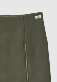 Gonna a matita verde scuro realizzata in tessuto liscio, con una zip laterale argentata e un'etichetta "Zero Waste Design" sulla vita.