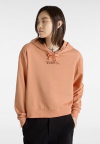 Sudadera coral clara de corte relajado, con capucha ajustable y el logo "vans." bordado. Tela suave y lisa con dobladillo acanalado.