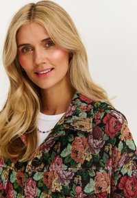 Denimowa kurtka w kwiatowy wzór z zielonymi, różowymi i pomarańczowymi różami na czarnym tle; ma kołnierz i widoczne przednie kieszenie.