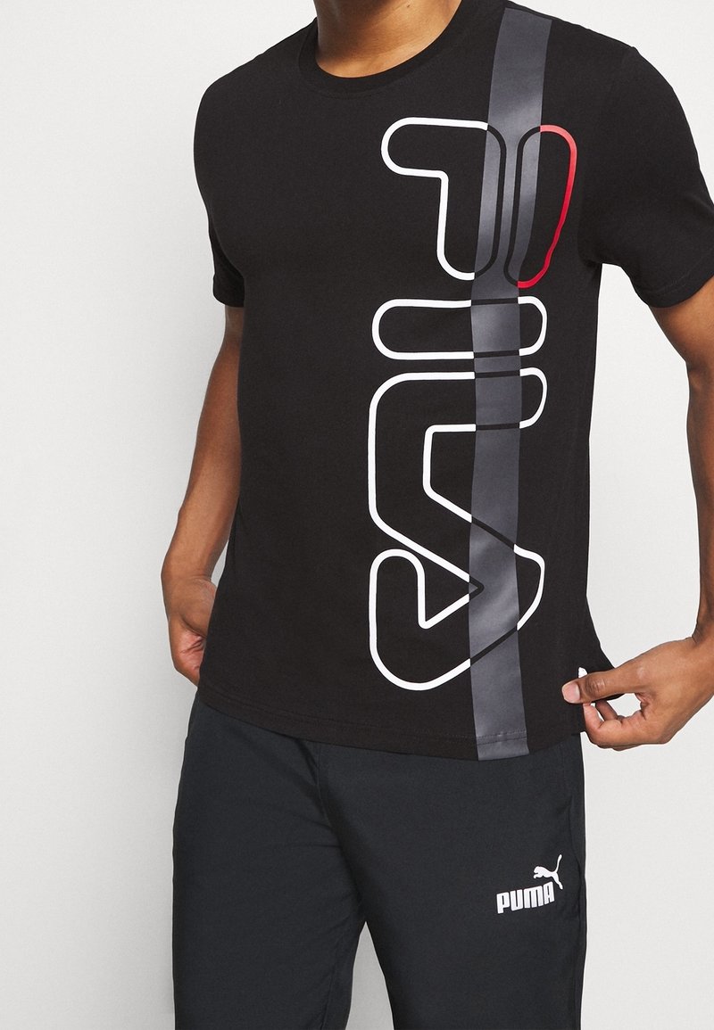 T-shirt en coton noir avec un grand motif graphique blanc et une bande verticale grise avec des accents rouges. Manches courtes et col rond.
