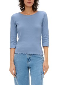 Lichtblauw geribbeld topje met driekwart mouwen, gekartelde zoom en aansluitend ontwerp, gecombineerd met lichtblauwe denim broek.