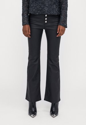 Zwarte uitlopende broek van een gladde, glanzende stof met een hoge taille en drie metalen knopen. Gecombineerd met puntige zwarte hoge hakken.