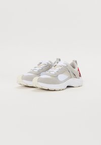 Graue und weiße Sneakers, die eine Mischung aus Wildleder und Mesh-Materialien aufweisen, eine dicke Sohle haben und rote Akzente an der Ferse besitzen. Die Schnürsenkel sind weiß.
