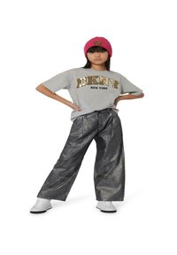 Camiseta de manga corta gris con el texto dorado "DKNY NEW YORK", combinada con pantalones anchos metálicos negros y zapatillas blancas. Se incluye un gorro de punto rosa.
