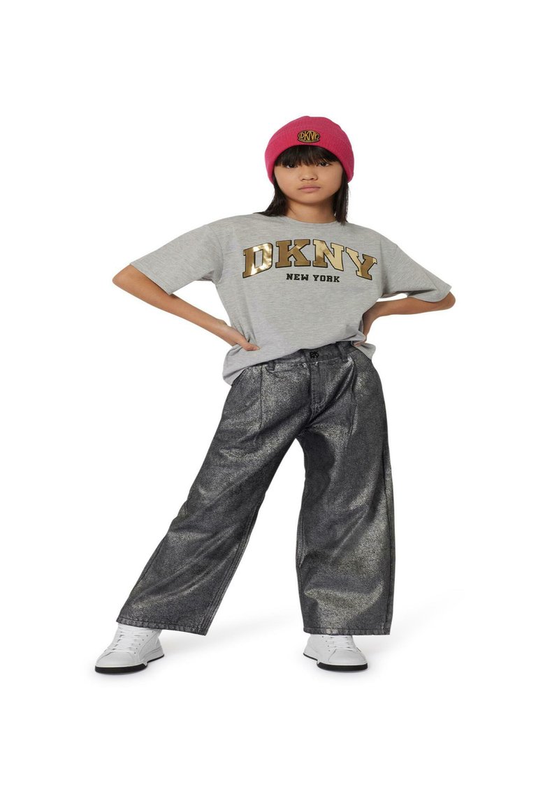 Camiseta de manga corta gris con el texto dorado "DKNY NEW YORK", combinada con pantalones anchos metálicos negros y zapatillas blancas. Se incluye un gorro de punto rosa.