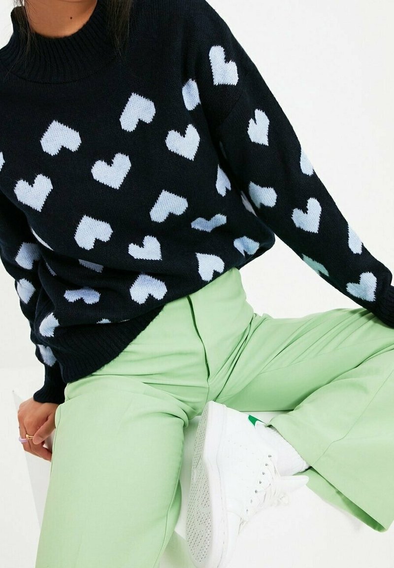 Svart tröja med ljusblå hjärt-mönster, ribbad halsringning, kombinerad med mintgröna byxor och vita sneakers. Tröjan har en avslappnad passform.