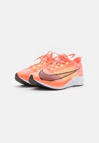 Baskets légères avec une tige respirante de couleur pêche-orange, un logo swoosh noir et une semelle extérieure contrastante en blanc et noir.