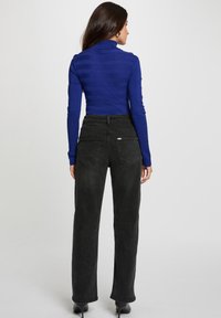 Maglione a collo alto a righe blu abbinato a jeans neri a vita alta, con due tasche posteriori e orlo pulito. Inclusi tacchi a spillo neri.