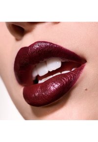 Lèvres d'un bordeaux profond avec une finition brillante, révélant une texture lisse et des dents blanches. Gros plan, mettant en avant les contours des lèvres.