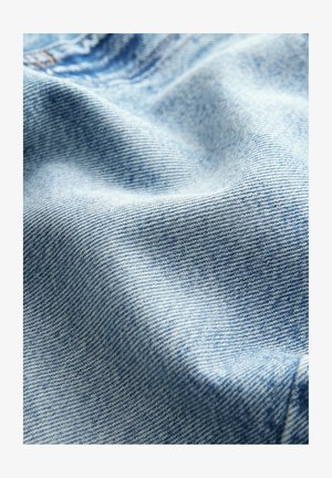 Světle modrá denimo látka s jemnou texturou, která má decentní keprový vzor a přirozené skladové linie.