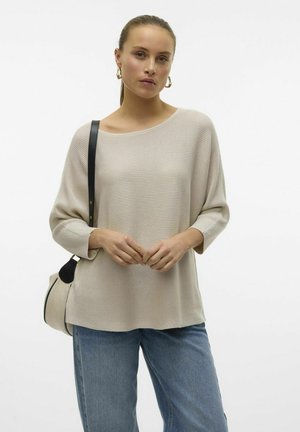 Maglione beige a maglia con scollo ampio e maniche a tre quarti, abbinato a jeans azzurri chiari e una borsa con un accento nero.