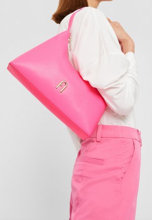 Mujer con blusa blanca y pantalones rosas lleva un bolso de hombro rosa brillante con cierre dorado.