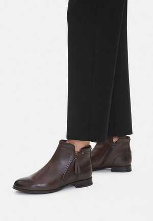 Braune Leder-Stiefeletten mit rund zulaufender Spitze, seitlichem Reißverschluss und Quasten-Detail. Kombiniert mit schwarzer Hose für eine schlanke Silhouette.