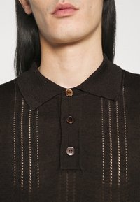 Hnědá pletená polo košile s límečkem a třemi knoflíky, s vertikálními pruhovanými výřezy, texturovanou tkaninou a slim fit střihem.