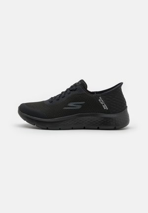 Scarpa sportiva nera con tomaia in mesh traspirante, dettagli texturizzati e suola ammortizzata. Presenta una punta arrotondata e design con lacci.