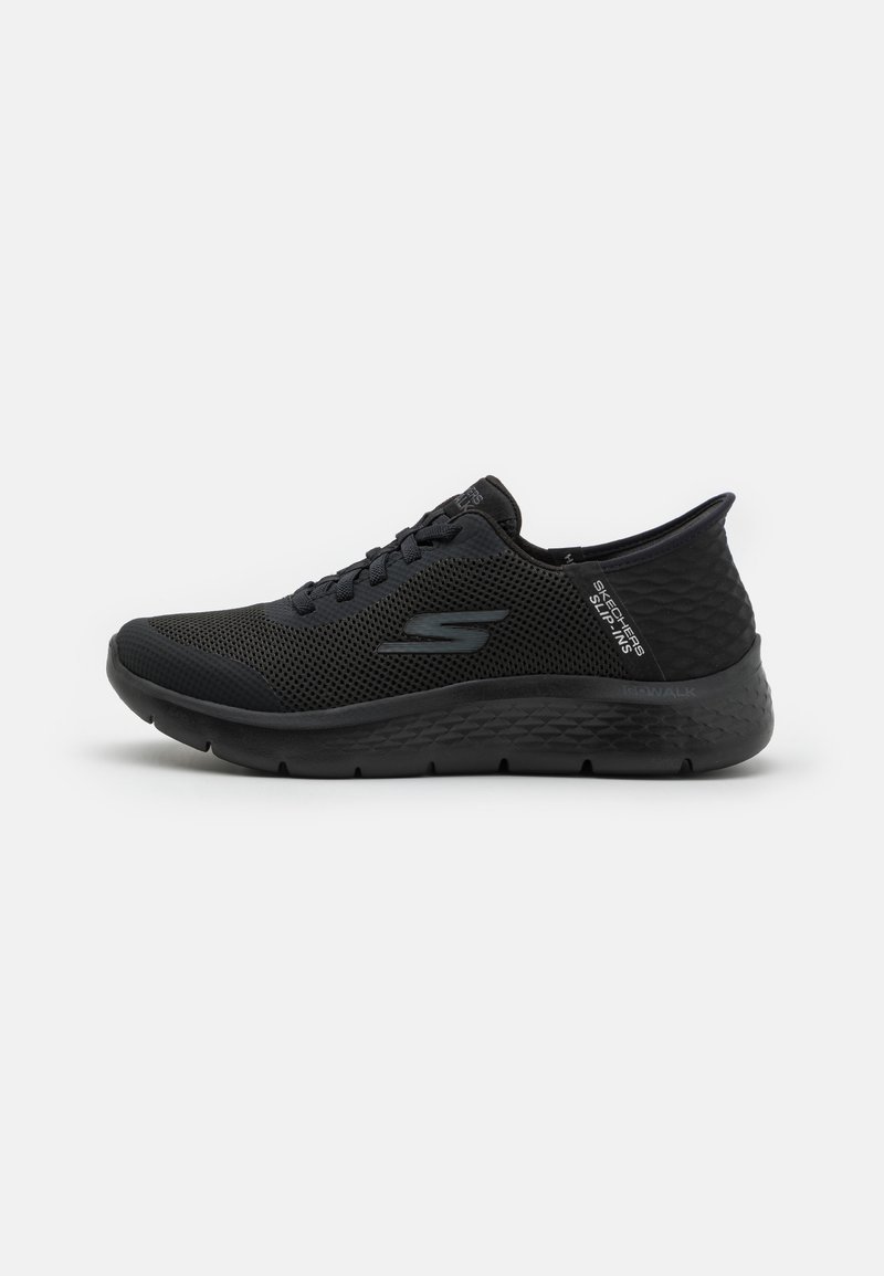 Zapatilla deportiva negra con parte superior de malla transpirable, acentos texturizados y suela acolchada. Presenta una punta redondeada y diseño con cordones.