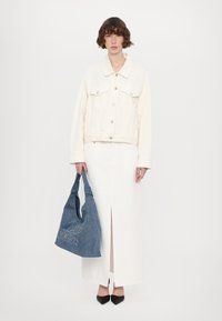 Kremfarget denimjakke med to brystlommer, kombinert med en hvit lang skjørt med frontsplitt. Holder en blå denim handlenett med søm detaljer.