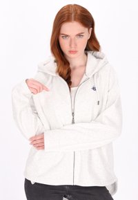 Lichtgrijze hoodie met rits en capuchon, voorzien van een zachte textuur, lange mouwen en een klein blauw logo op de linkerborst.