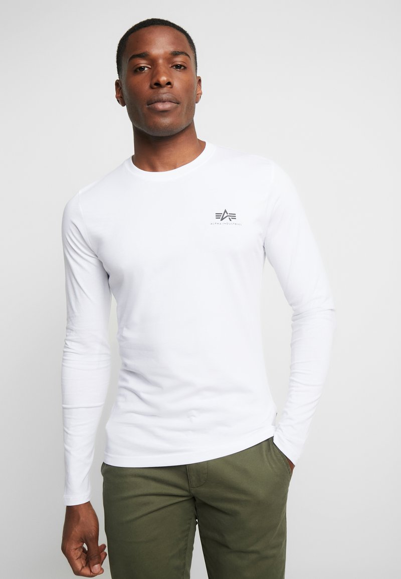 Langærmet hvid T-shirt lavet af bomuld, med et lille gråt logo på brystet. Glat tekstur, rund halsudskæring og tætsiddende design.