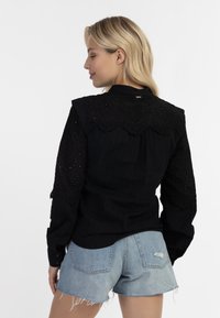 Zwarte shirt met oogjesafwerking op de schouders en mouwen, textuurstof, knoopmanchetten, gecombineerd met lichtblauwe denim shorts. Casual fit.