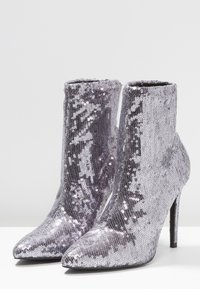Botas de tobillo cubiertas de lentejuelas con punta afilada, tacón de aguja y un color plateado brillante. Diseño elegante con altura ajustada en el tobillo.