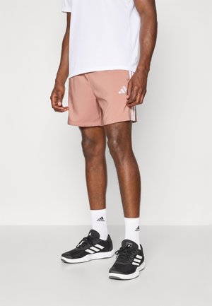 Lyse rosa treningsshorts med hvite sidestriper og Adidas-logo. Komplimentert av svarte sko og hvite sokker. Enkel design.