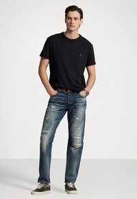 Μαύρο βαμβακερό μπλουζάκι με τσέπη στο στήθος και κόκκινο λογότυπο, συνδυασμένο με μπλε τζιν τζιν με σκισίματα και patches. Καθημερινά sneakers με κορδόνια.