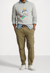 Grå худі med en björnillustration och färgglad "Polo" text, lagd över en ljusblå chambray-skjorta och tillsammans med khaki cargo-byxor.