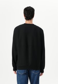 Felpa nera con una vestibilità rilassata, colletto a girocollo e maniche lunghe. Realizzata in tessuto morbido, presenta un design semplice e senza motivi visibili.
