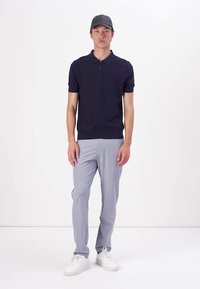 Mørkeblå kortermet polo med glidelås krage, kombinert med lysegrå bukser og hvite joggesko. Modellen har på seg en matchende grå caps.