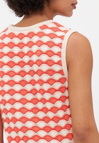 Débardeur en tricot sans manches présentant un motif ondulé corail et crème, fabriqué à partir d'un tissu doux avec une finition texturée et un col rond.