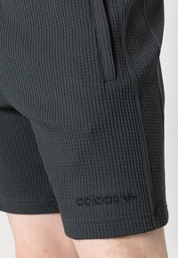Černé šortky s texturou vafle a elastickým pasem, se bočními kapsami a embosovaným logem "adidas" na levém lemu.