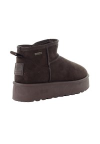 Brązowy zamszowy botek za kostkę z płaską, fakturowaną podeszwą, wyposażony w tylną pętlę do ściągania oraz naszywkę z logo z boku. Gładka cholewka z przeszyciami.