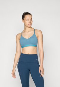 Plava sportska majica s tankim naramenicama, V-izrezom i Nike logotipom na elastičnom pojasu. Uparena s hlačama od tamnoplavog najlona s visokim strukom.
