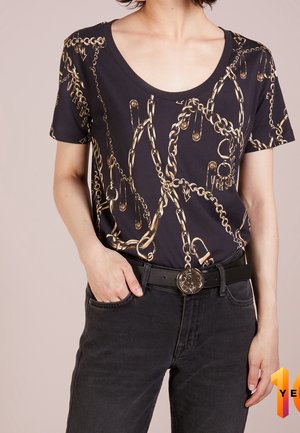 Sort T-shirt med print af guldkæde og sikkerhedsnål, med en bred, rund halsudskæring. Kombineret med sorte jeans og et bælte med en rund metalspænde.