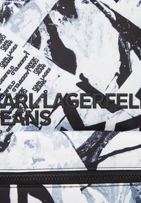Tela de patrón en blanco y negro con "KARL LAGERFELD JEANS" grabado en goma negra. Textura suave con un diseño geométrico. Cierre con cremallera.
