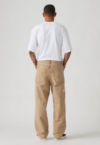 Bež hlače cargo s sproščenim krojem, dvema stranskima žepoma in standardnima zadnjima žepoma. Nošene z enostavno belo majico s kratkimi rokavi.