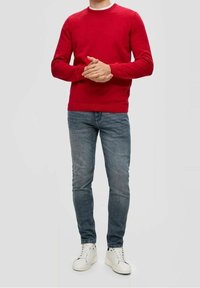 Rode gebreide trui met een ronde hals, gecombineerd met lichtblauwe slim-fit jeans en witte sneakers. Binnenlandse studio achtergrond.