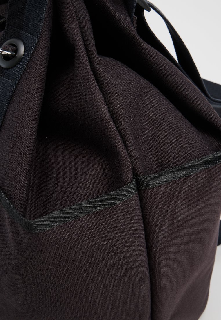Bolsa de lona negra con una superficie texturizada, presenta dos acentos horizontales y asas resistentes para llevar.