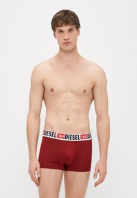 Červené bavlnené boxerky s čiernym a bielym opaskom s logom značky. Materiál je hladký, s priliehavým strihom a krátkym nohavičkovým strihom.