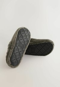 Szare kapcie wyściełane futrem z teksturowaną czarną gumową podeszwą z geometrycznym wzorem, charakteryzujące się zaokrąglonym kształtem i miękkim wykończeniem.