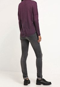 Lila Langarmoberteil mit lockerer Passform, kombiniert mit schmalen, dunkelgrauen Jeans und schwarzen Schnürschuhen. Strukturiert, lässiges Design.