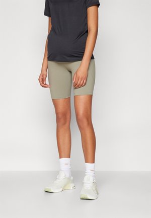 Pantalones cortos de ciclismo gris claro combinados con una camiseta oscura; el calzado presenta detalles en blanco y verde claro con tejido texturizado; calcetines blancos de longitud media.