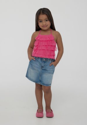 Top halter rosa arricciato con gonna di denim, entrambi stili casual. L'outfit è completato da scarpe piatte rosa, in piedi contro uno sfondo bianco.