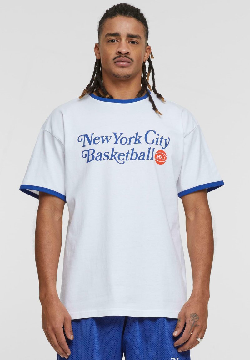 Hvit bomull t-skjorte med blå kant, med «New York City Basketball»-grafikk i blått. Båret med blå mesh-shortser.