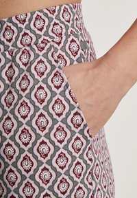 Patroon stofbroeken met een gedempte teal basis en bordeauxrode en roze bloemmotieven. Zichtbaar detail van zijzakken. Soepele textuur.