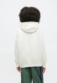 Sweatshirt oversize de cor creme com capuz e cordão, punhos e bainha canelados. Textura de tecido lisa, vista traseira mostra detalhes mínimos e sem estampas.