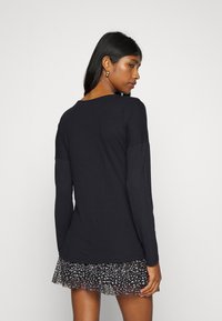 Blusa preta de mangas compridas, feita de um tecido suave, com um decote arredondado. Combinada com uma saia curta e com volantes, com um padrão abstrato em preto e branco.