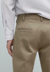 Gråstribet skjorte med knapmanchetter, parret med lysebrune bukser. Bukserne har baglommer med en glat tekstur og en skræddersyet pasform.